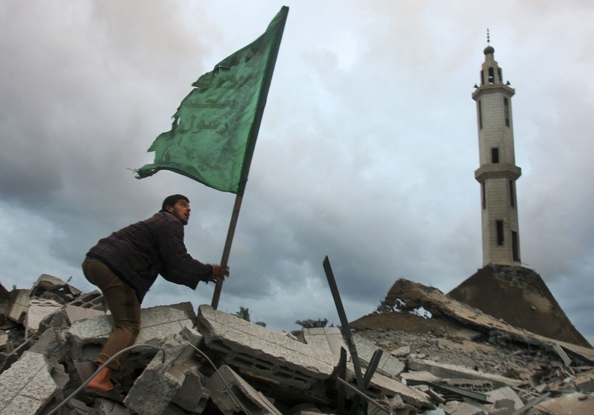 A Palestinian man places a green Islamic flag used by the militant group Hamas on the rubble of a destroyed mosque after an Israeli airstrike in Gaza City, Wednesday. (The Spokesman-Review)