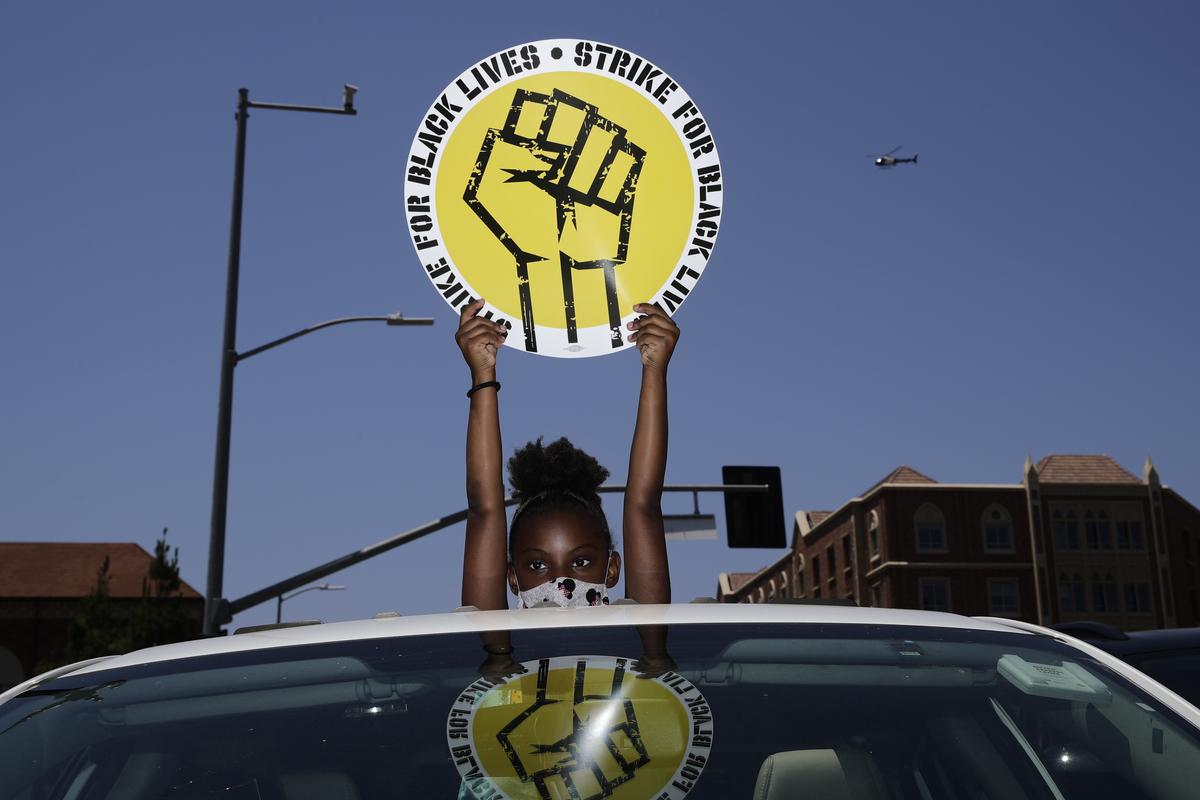 FILE - In this July 20, 2020, file photo, Audrey Reed, 8, holds up a sing through the sunroof of a car during a rally in Los Angeles. Ahead of Labor Day, major U.S. labor unions say they are considering work stoppages in support of the Black Lives Matter movement. (Jae C. Hong)