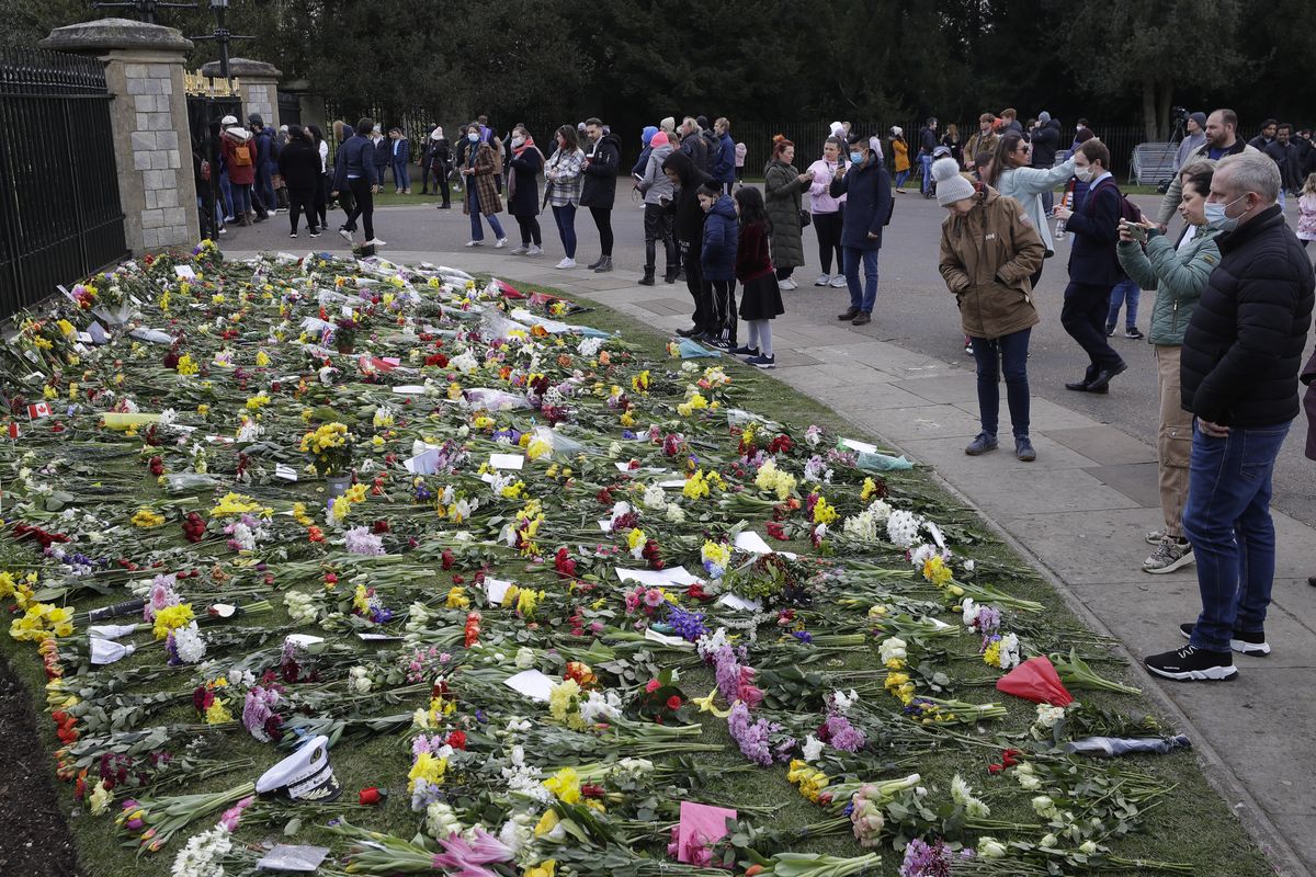 People look at flowers outside Windsor Castle in Windsor, England Sunday, April 11, 2021. Britain's Prince Philip, the irascible and tough-minded husband of Queen Elizabeth II who spent more than seven decades supporting his wife in a role that mostly defined his life, died on Friday.  (Kirsty Wigglesworth)