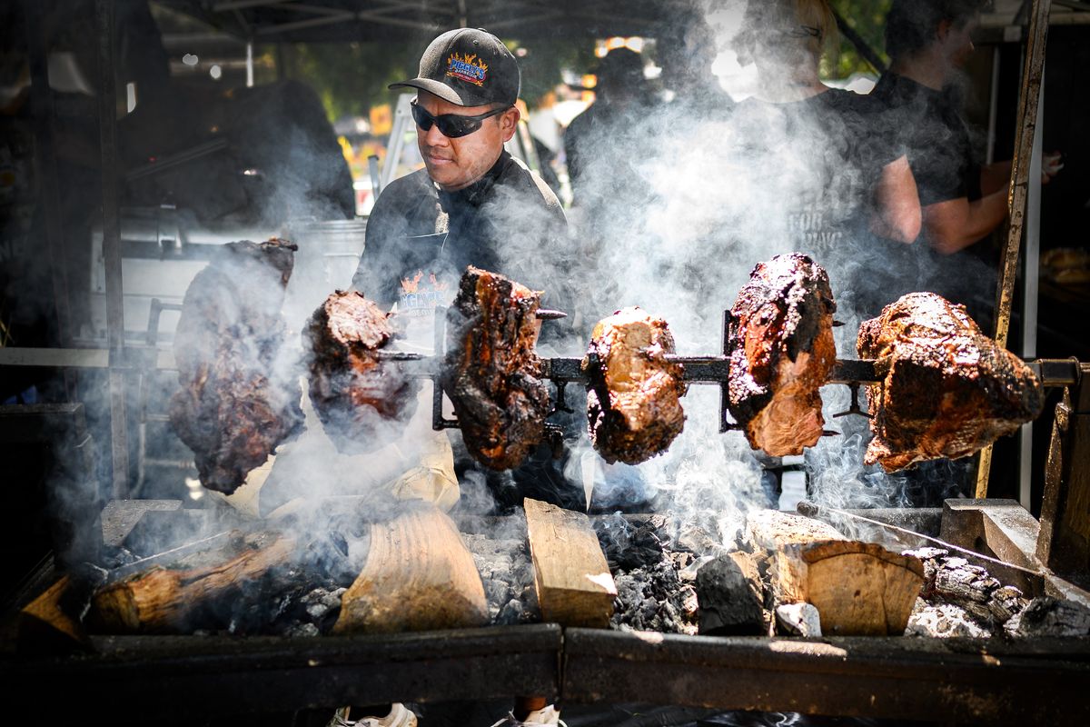 Jesus Andrade with Piggly’s BBQ adds mesquite charcoal underneath roast beef rotating on a spit in this August 2019 photo at Pig Out in the Park in Spokane.   (COLIN MULVANY)