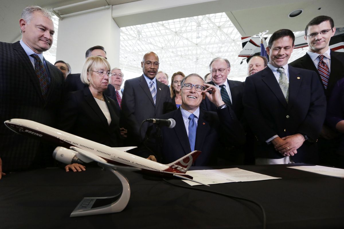 Gov. Jay Inslee, center, adjusts his glasses as he prepares to sign legislation to help keep production of Boeing’s new 777X in Washington on Monday at the Museum of Flight in Seattle. The legislation that was passed Saturday at a special session in Olympia extends tax incentives for Boeing to 2040 and directs millions of dollars to training programs for aerospace workers. (Associated Press)