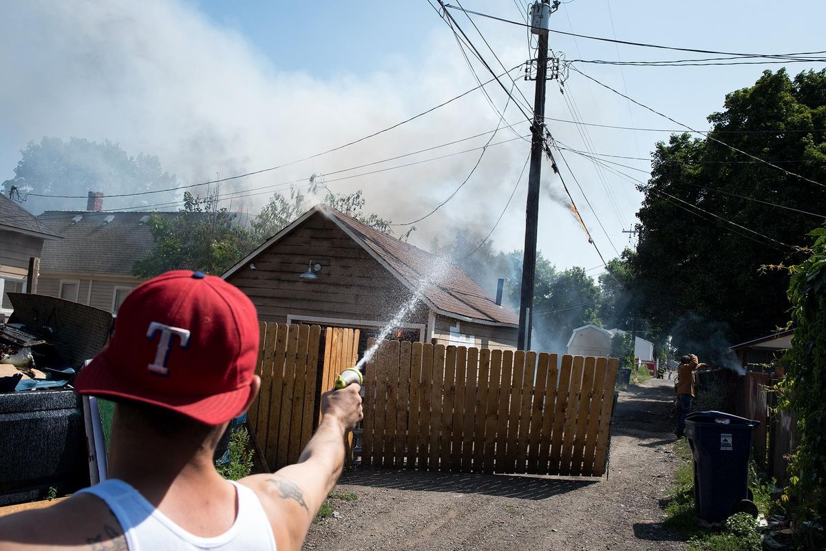 Brent Lerma douses his neighbor’s fence on July 19, 2019. The fire burned a garage and part of a home on the 2300 block of West Mallon. (Eli Francovich / The Spokesman-Review)
