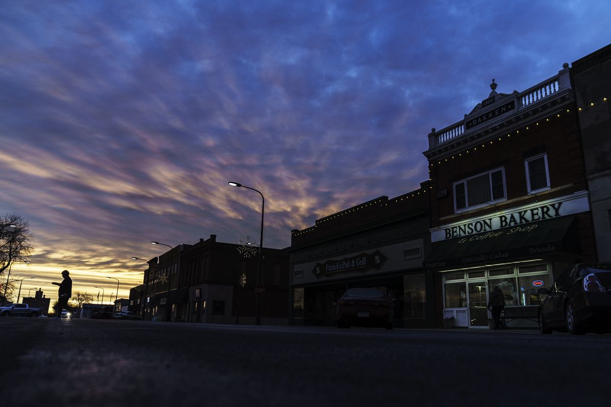 A customer carries a box of baked goods from a bakery at sunrise in Benson, Minn., Wednesday, Dec. 1, 2021. One little town. Three thousand people. Two starkly different realities. It
