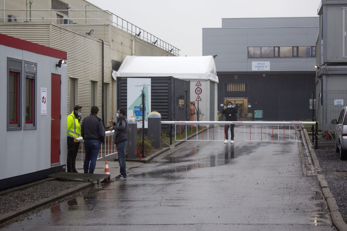 A security guard talks to people at the entrance of Novasep factory in Seneffe, Belgium, Thursday, Jan. 28, 2021. Belgian health authorities said Thursday they have inspected a pharmaceutical factory located in Belgium to find out whether the expected delays in the deliveries of AstraZeneca