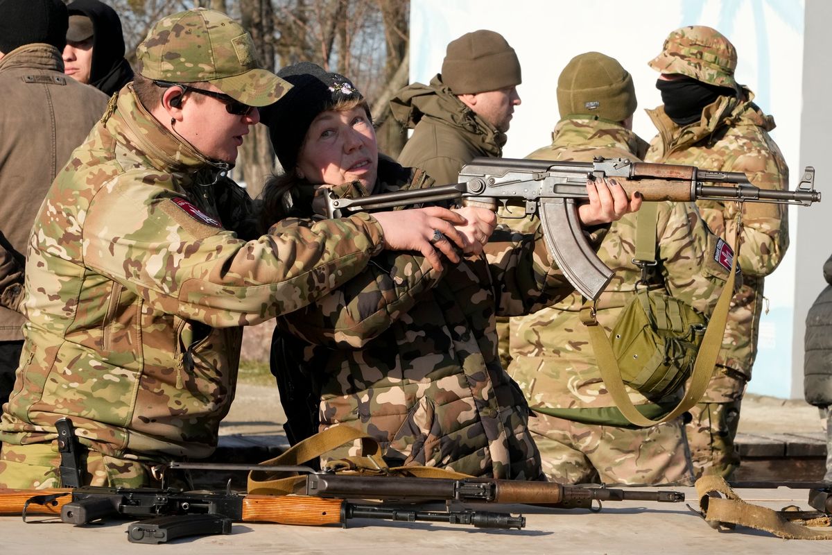 An instructor shows a woman how to use a Kalashnikov assault rifle, as members of a Ukrainian far-right group train, in Kyiv, Ukraine, Sunday, Feb. 13, 2022. Russia denies it intends to invade but has massed well over 100,000 troops near the Ukrainian border and has sent troops to exercises in neighboring Belarus, encircling Ukraine on three sides. U.S. officials say Russia