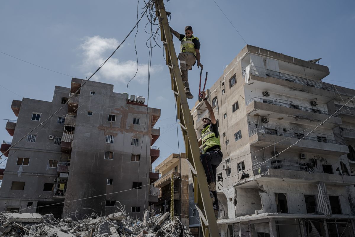 Civil defense workers cut fallen power lines as they clean up amid buildings destroyed in recent Israeli strikes on Friday in Tyre, Lebanon. (DANIEL BEREHULAK)