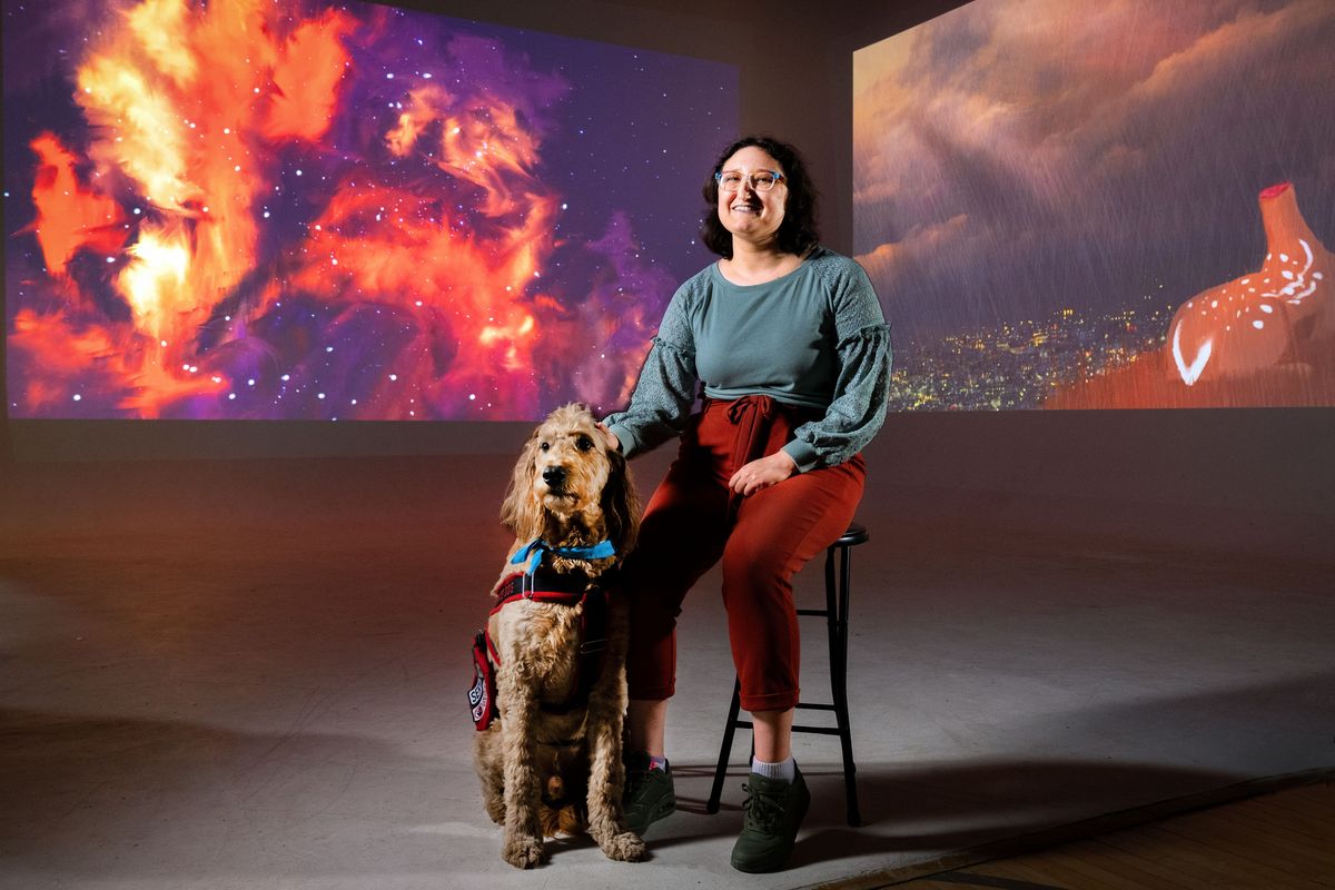 Emilija Blake, with her guide dog Kasper, sits in front of her projected digital artworks as part to her show, “The World Between.” The multimedia presentation focuses primarily on the unique challenges of life as a disabled person. The show opens 6 to 9 p.m. Friday and runs 11 a.m.-3 p.m. Saturday and Sunday.  (COLIN MULVANY/THE SPOKESMAN-REVIEW)