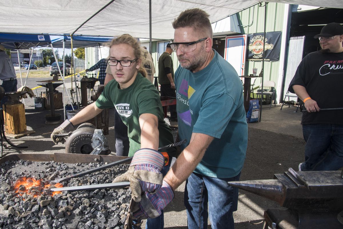 Alexander Carlson, 16, left, gets a helping hand from his dad, Clayton Carlson , as the pair participate in the Columbia Fire and Iron hammer-in blacksmith event, Sunday, Oct. 8, 2017, at Morgan Jade Ironworks in Spokane, Wash. Alexander, a first-timer, made shoe and bike hooks while Clayton worked on a fireplace poker. Over 100 blacksmiths hammered on iron using 14 anvils and 7 forges. (Dan Pelle / The Spokesman-Review)