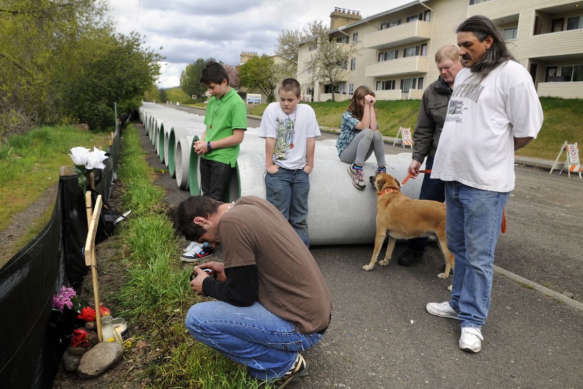 After placing a homemade cross at the site, Michael Zachman, front left, Kai Jensen, with dog, and Weston Taylor, far right, gather with neighborhood children Friday to say a prayer in memory of Sharlotte McGill at the corner of Magnolia Street and South Riverton Avenue in Spokane, where McGill was fatally attacked. (Dan Pelle)