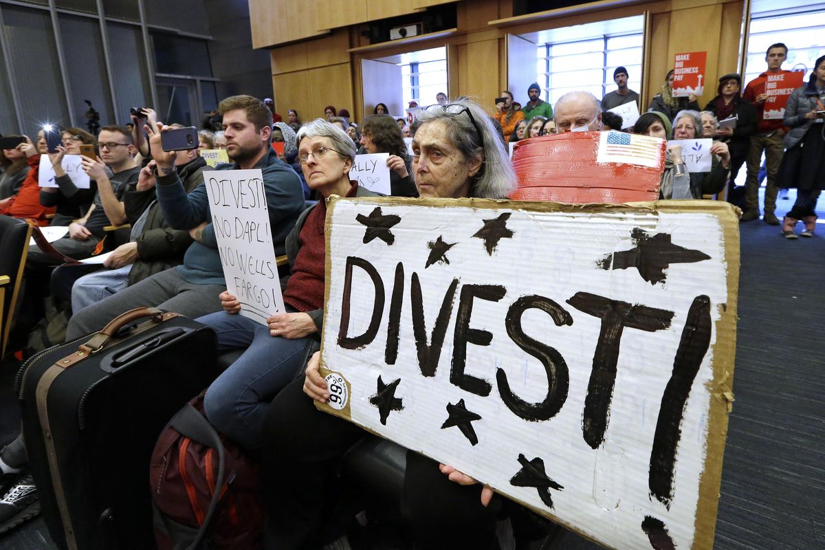 Cynthia Lynet holds a sign Tuesday in favor of divestiture during a Seattle City Council meeting before a scheduled vote on whether to divest $3 billion in city funds from Wells Fargo over its funding of the Dakota Access Pipeline. (Elaine Thompson / Associated Press)