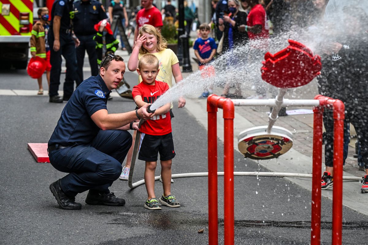 Spokane firefighter/paramedic Shawn Monaghan helps youngsters hit a target with a fire hose during the Junior Fire Academy, Sunday, Sept. 17, 2023, in downtown Spokane. The Spokane Fire Department, SAFE Kids Spokane, the Downtown Spokane Partnership and River Park Square partnered for the 5th annual event.  (DAN PELLE/THE SPOKESMAN-REVIEW)