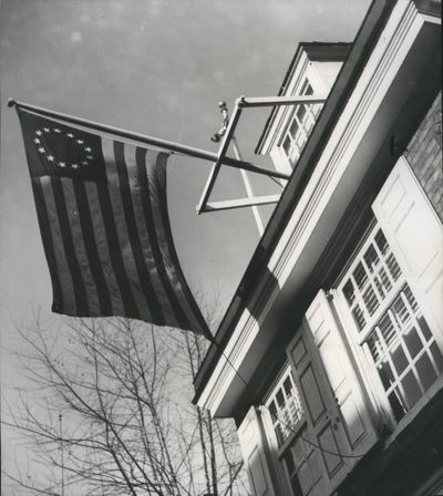 A replica of the first Stars and Stripes hangs outside what is labeled the Philadelphia home of Betsy Ross, in this undated photo. Many historians dispute that Ross actually lived in the home. The stripes and stars symbolize the first 13 states, and their names in large part reflect the prerogative of the English monarchy in the 17th century.   (Metro News)