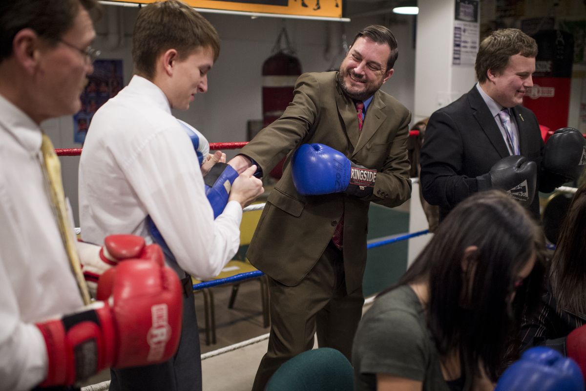 Rogers senior Zackary Bonser helps Spokane City Council President Ben Stuckart into a boxing glove on Tuesday at The Howard Street Gym in Spokane. They were preparing for Rhetoric in the Ring, a debate event to support the Rogers High School debate team. (Tyler Tjomsland)