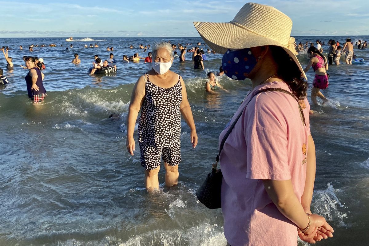 Women wearing face masks stand on a beach in Vung Tau city, Vietnam, Sunday, July 26, 2020. Vietnam on Sunday reimposed restrictions in one of its most popular beach destinations after a second person tested positive for the virus, the first locally transmitted cases in the country in over three months.  (Hau Dinh)