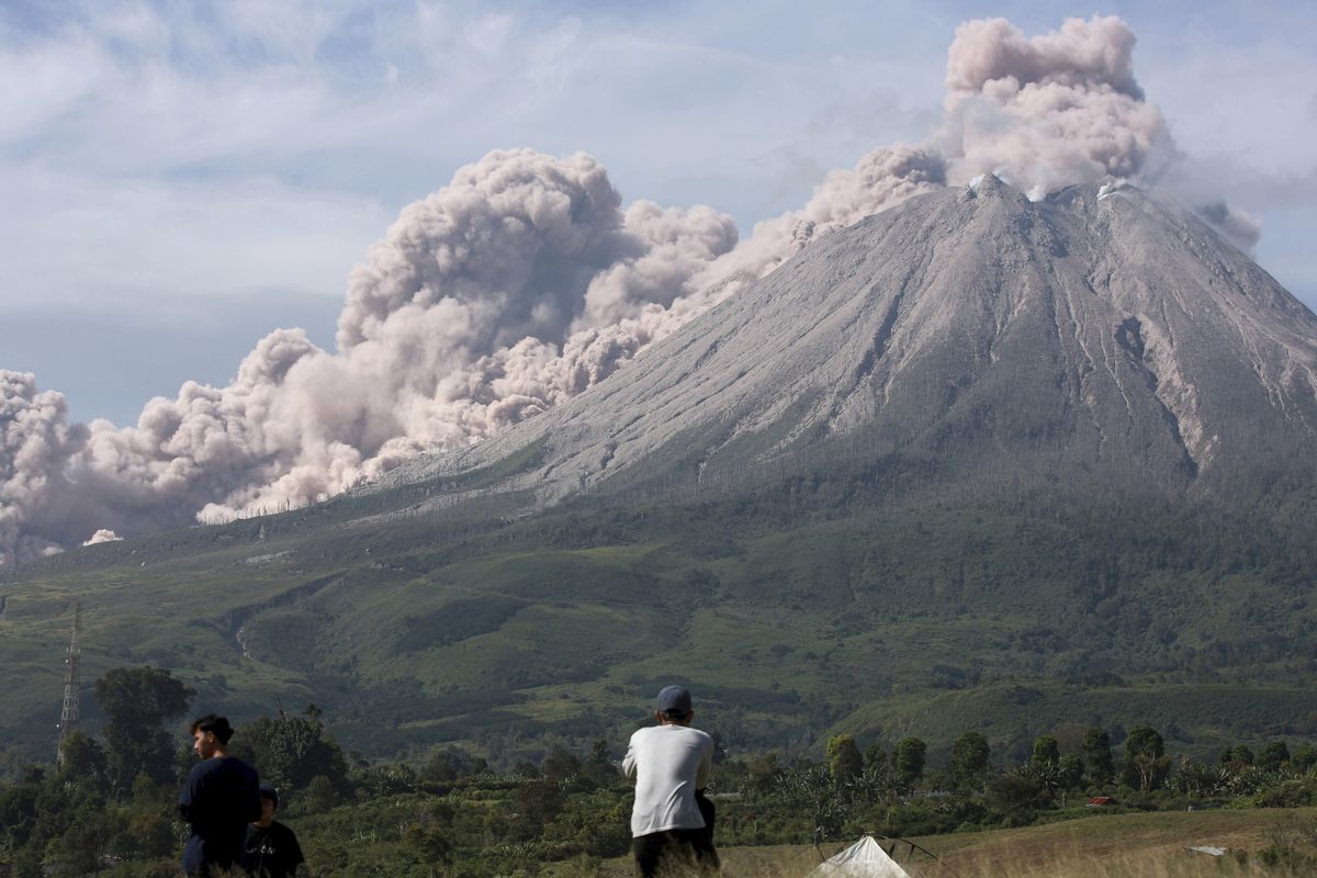 People watch as Mount Sinabung spews volcanic materials during an eruption in Karo, North Sumatra, Indonesia, Thursday, March 11, 2021. The volcano unleashed an avalanche of searing gas clouds flowing down its slopes during eruption on Thursday. No casualties were reported.  (Binsar Bakkara)