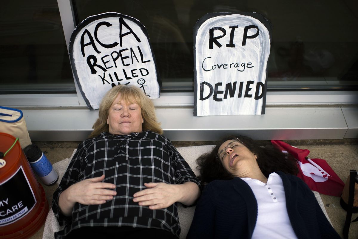 Maureen Quinn, left, and Maria Palmer pretend to be dead as protestors gather before a town hall held by New Jersey Republican Rep. Tom MacArthur in Willingboro, N.J., Wednesday, May 10, 2017. (Joe Lamberti / Camden Courier-Post via AP)