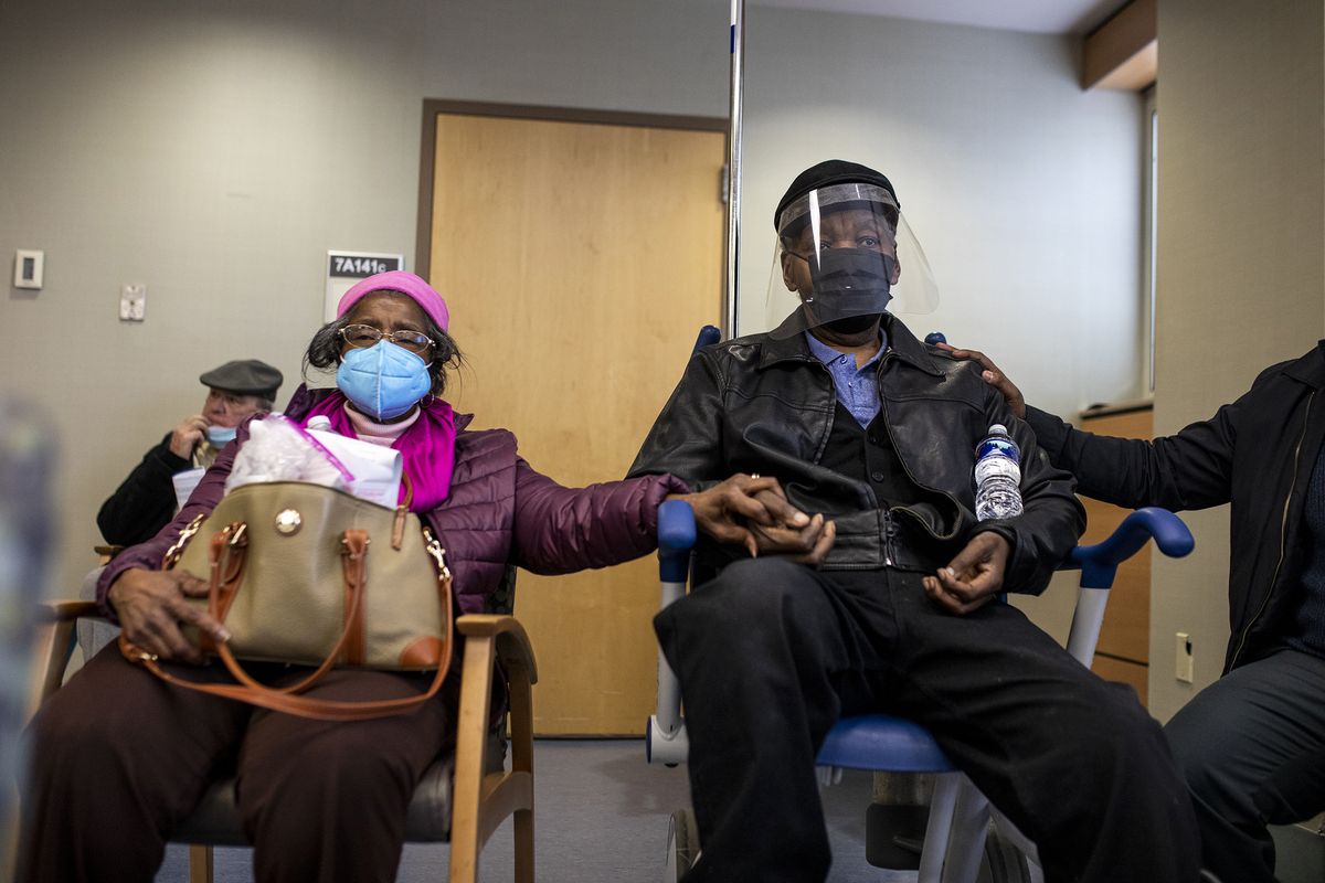 Dorothy Kade holds the hand of her husband, Walter Kade Jr., as they wait Saturday in the observation room after he received a COVID-19 vaccine at the VA Medical Center in Philadelphia.  (Tyger Williams)