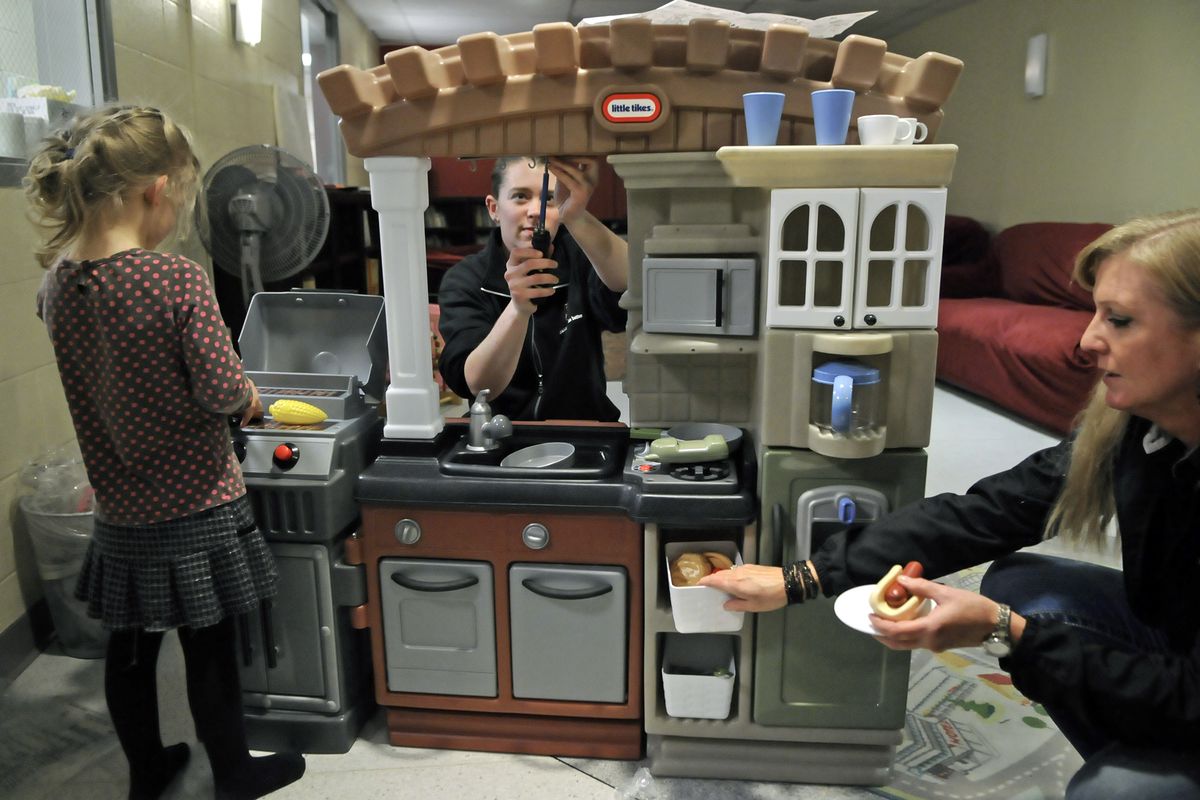 Sharaya Pearson, center, and Sheila Geraghty assemble a toy kitchen as a child in the care of Sally’s House plays with the grill section Friday at the receiving care center in Spokane. A private donation paid for the new kitchen set. (phOTOS BY DAN PELLE)
