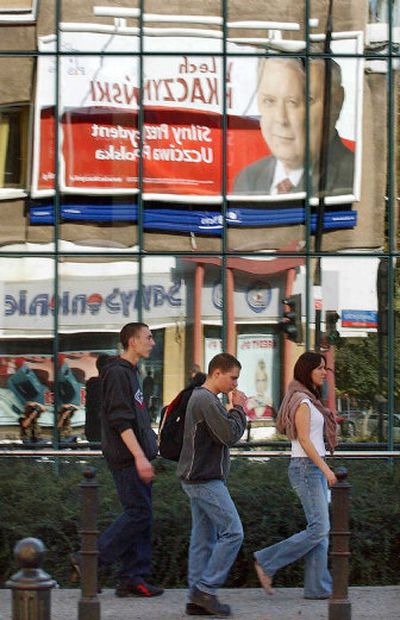 
People walk past the glass of a building with a reflection of a poster promoting presidential candidate Lech Kaczynski in Warsaw on Saturday. 
 (Associated Press / The Spokesman-Review)