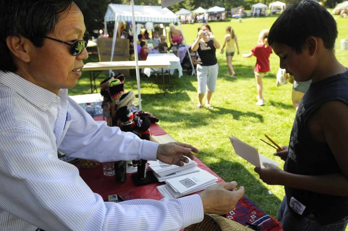 Vangtou Xiong Toyed, who is Hmong but now a U.S. citizen, stamps visitors’ “passports”  at the Cultural Village at  Unity in the Community. (Jesse Tinsley / The Spokesman-Review)