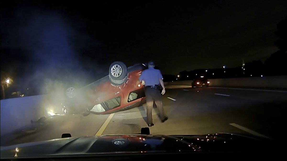 This screen shot taken from dash cam video owned by the Arkansas State Police shows trooper Rodney Dunn walking toward a flipped car in Pulaski County, Ark., on July 9, 2020. An Arkansas woman is suing the state police after she says a trooper crashed into her car, causing it to flip, after she didn