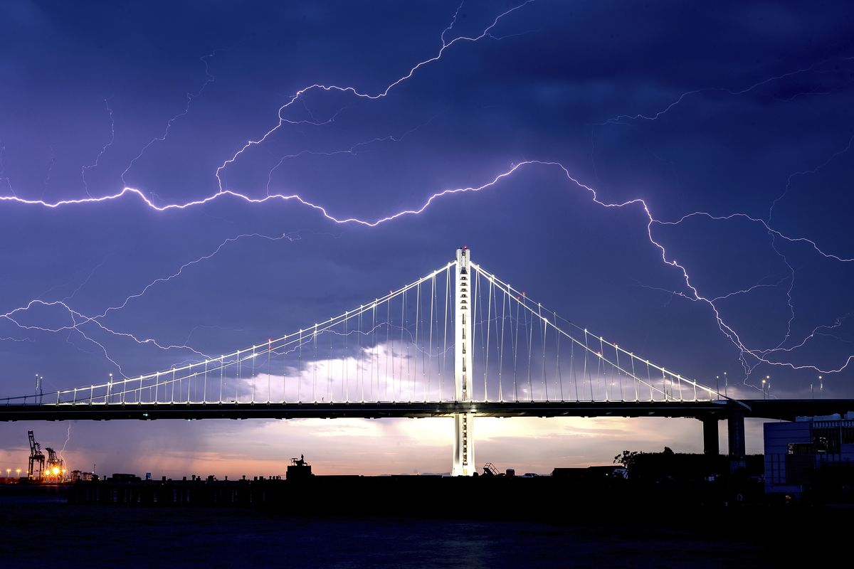 FILE - In this Aug. 16, 2020, file photo, lightning forks over the San Francisco-Oakland Bay Bridge as a storm passes over Oakland, Calif. Numerous lightning strikes sparked brush fires throughout the region.  (Noah Berger)