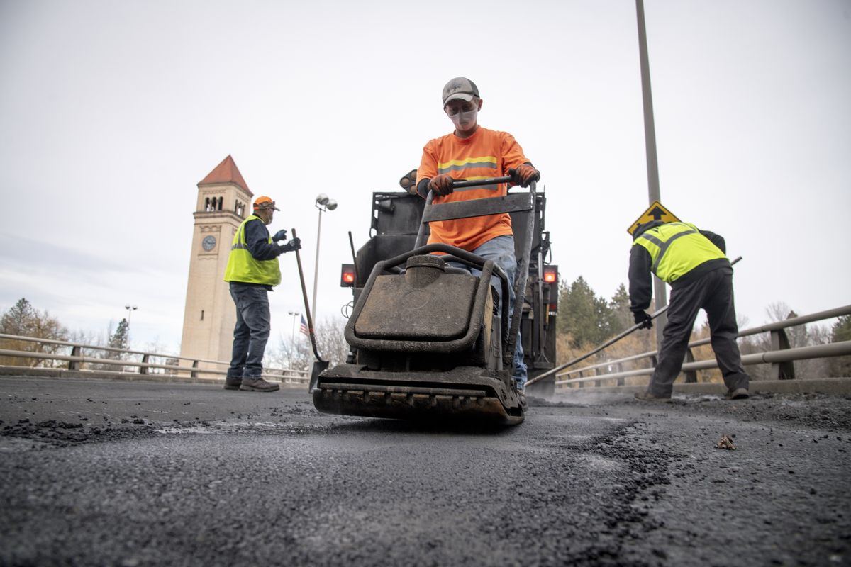Street Department worker Kelly Stevens, center, uses a machine to pack asphalt mix into a pothole Friday while Alex Mizner, left, and Tom Daves fill more holes in the road surface on Washington Street, north of Spokane Falls Boulevard. Midwinter pothole repair requires heating up cold patch materials to help it adhere to the roadway.  (Jesse Tinsley/THE SPOKESMAN-REVIEW)