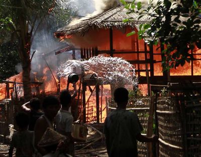 A person throws a bucket of water at a house engulfed in flames in Sittwe, Myanmar, on Monday. (Associated Press)