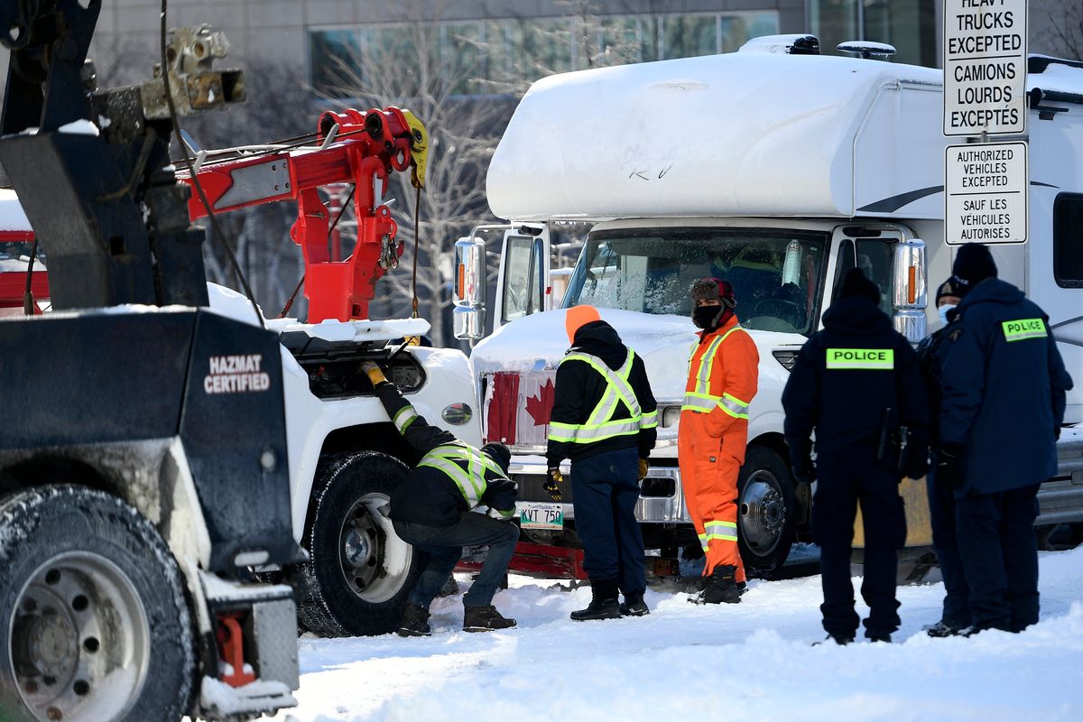 Police officers assist a tow operator to remove a truck from a blockade on Nicholas St. in Ottawa, on Friday, Feb. 18, 2022. Police began arresting protesters Friday in a bid to break the three-week, traffic-snarling siege of Canada