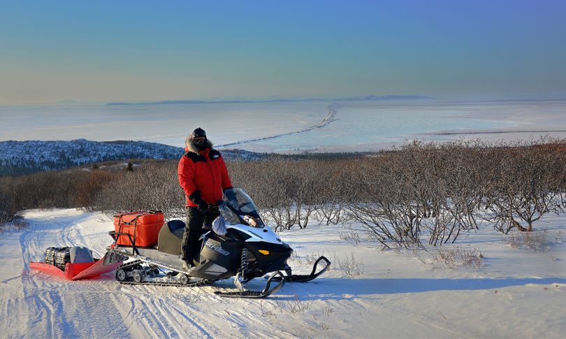 The Iditarod Trail passes over the high escarpment of the Blueberry Hills, which lie between Unalakleet  and Shaktoolik.  Immediately prior to dropping from the higher country and onto the beach, this view
presents itself. This long, narrow spit leading 15 miles off into the distance leads to Shaktoolik.  This spit separates the frozen ocean to the west (left) from the land/fresh water to the east (right).  The trail follows the spit toward the north.  Josh Rindal of Spokane and Bob Jones of Kettle Falls were snowmobiling 1,400-miles along the route of Alaska's famous Iditarod Sled Dog Race in March 2014.
 (Robert Jones)