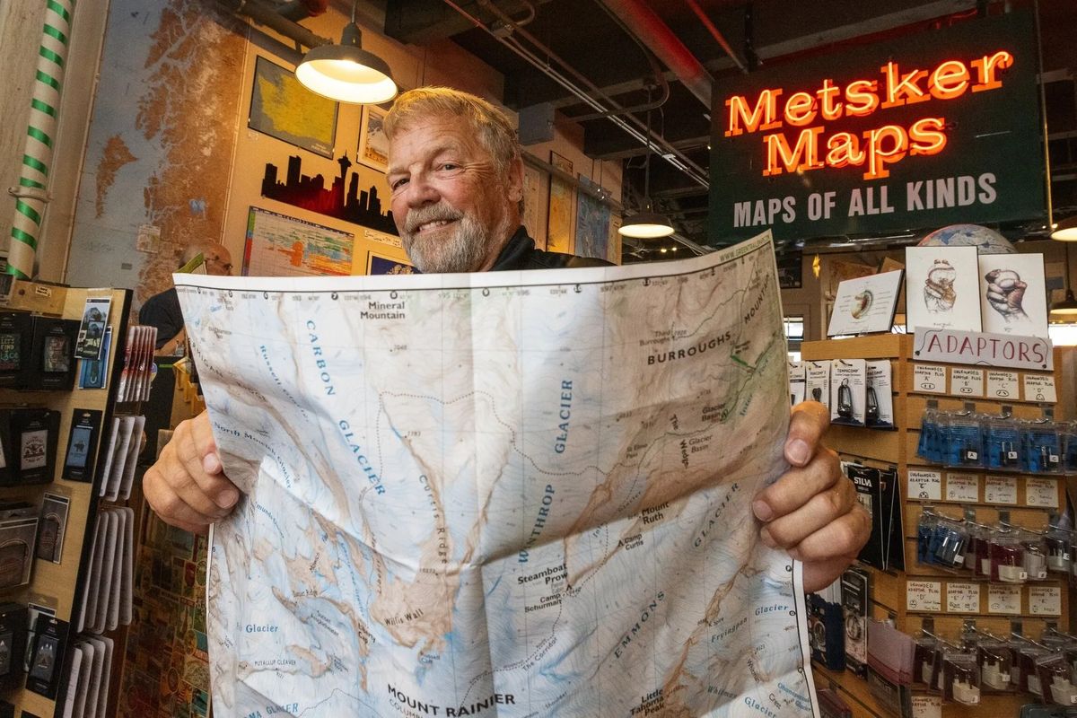 Alan Coburn, president of Green Trails Maps, holds a new revised edition of a map of Mount Rainier on Wednesday, Aug. 16, at Metsker Maps in Seattle. The map company turns 50; Metsker was the first retailer to carry them.  (Ken Lambert/The Seattle Times)