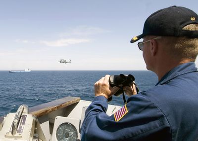 The commanding officer of a U.S. Navy guided-missile cruiser monitors the pirated Ukrainian cargo ship Faina off the coast of Somalia on Tuesday, while one of his helicopters provides surveillance.  (Associated Press / The Spokesman-Review)