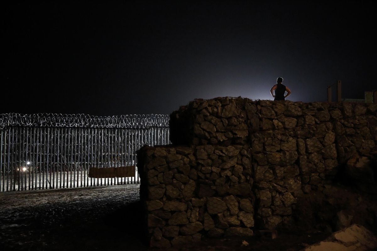 Floodlights from the U.S, illuminate the border wall, topped with razor wire, as a man exercises, right, Monday, Jan. 7, 2019, on the beach in Tijuana, Mexico. With no breakthrough in sight, President Donald Trump will argue his case to the nation Tuesday night that a "crisis" at the U.S.-Mexico border requires the long and invulnerable wall he