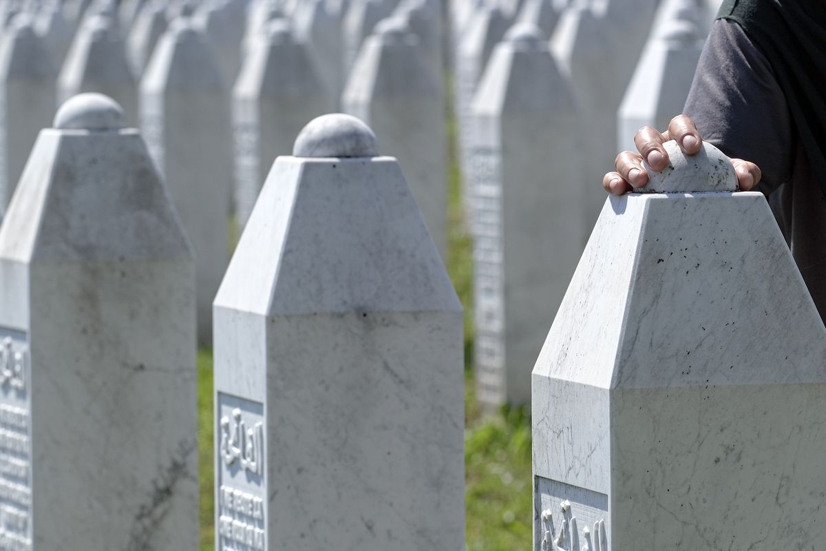 A woman touches a grave stone in Potocari, near Srebrenica, Bosnia, Saturday, July 11, 2020. Mourners converged on the eastern Bosnian town of Srebrenica for the 25th anniversary of the country