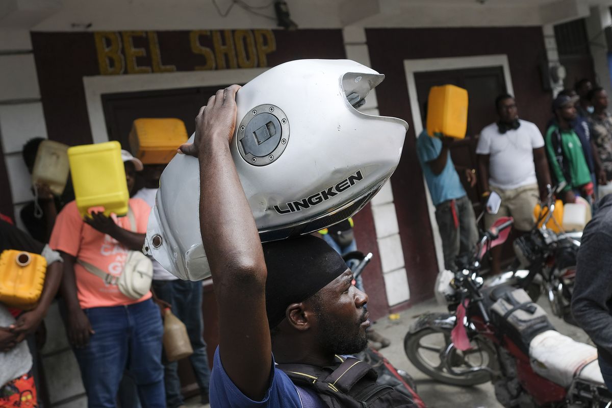 A man balances his motorbike tank on his head as he waits outside a gas station in hopes of filling his tank, in Port-au-Prince, Haiti, Saturday, Oct. 23, 2021. The ongoing fuel shortage has worsened, with demonstrators blocking roads and burning tires in Haiti