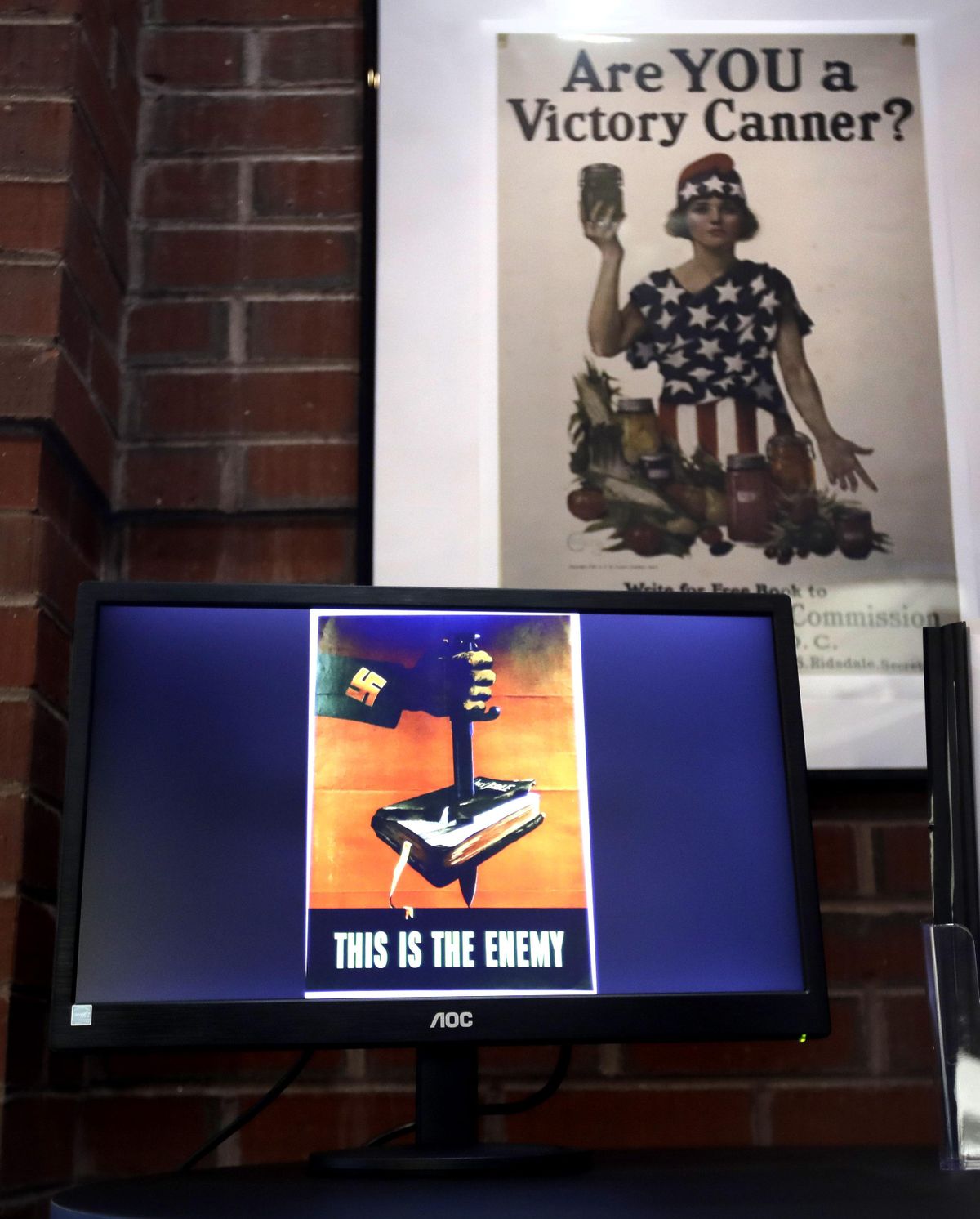 A National War Garden Commission poster copy hangs in a hallway as a display loop shows historic posters on monitor at the Rochester Public Library in Rochester, N.H., on Thursday, Nov. 8, 2018. A trove of propaganda posters from World War I and II were found recently found after being lost in storage for decades in the library’s basement. (Charles Krupa / AP)