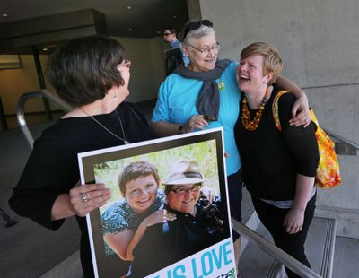 Victoria Smith Weiland, left, from Eugene, Ore., holds a picture of her and her partner Peggy McComb, as McComb hugs Aubrey Chonbold, right, on the steps of the Wayne L. Morse U.S. Courthouse Wednesday, May 14, 2014, in Eugene, Ore. A federal judge will hear arguments Wednesday about whether a national group can defend Oregon's ban on same-sex marriage because the state's attorney general has refused to do so. (Chris Pietsch / The Register-guard)