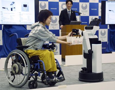 A robot passes a basket containing drinks to a woman in a wheelchair during an unveiling event in Tokyo Friday, March 15, 2019. (高橋伸輔 / AP)