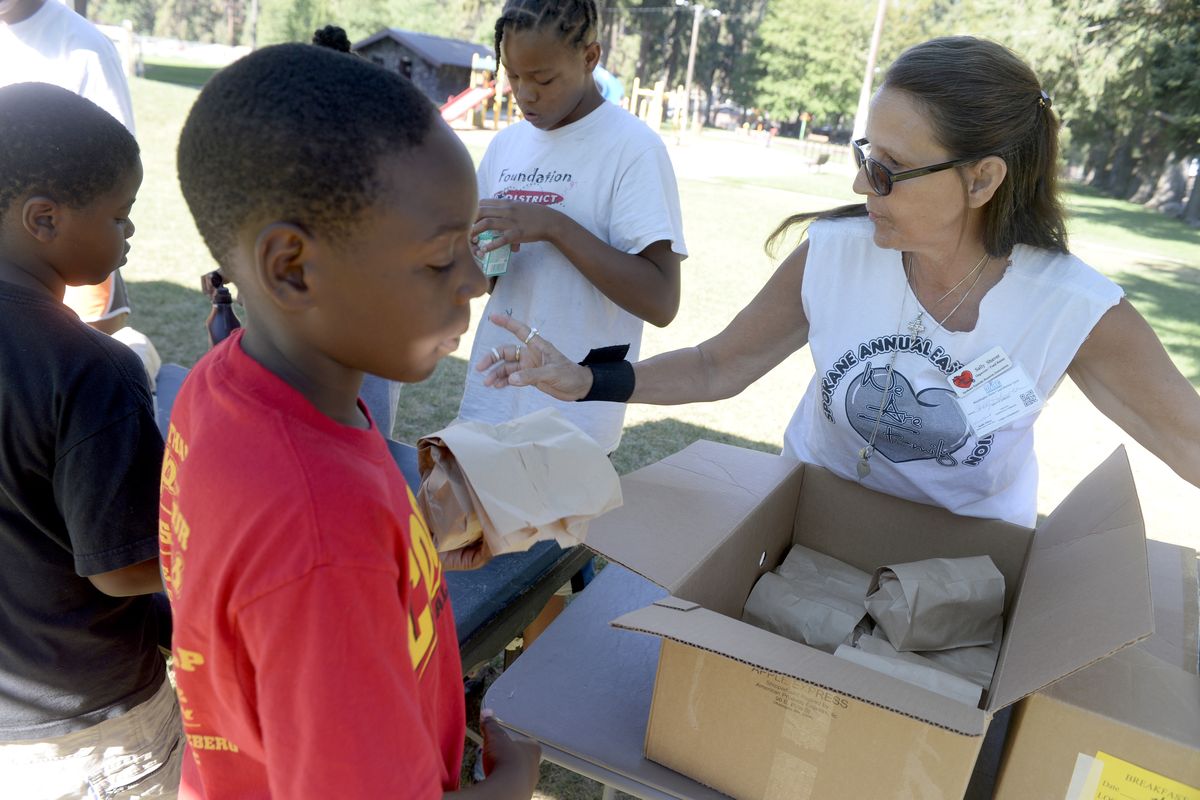 Sally Shaver, right, passes out breakfast at the Spokane Eastside Reunion Basketball Camp on Tuesday. Shaver is a volunteer and distributes food from the Rogers High School summer meals program and puts on arts and crafts classes for kids not playing basketball at the camp. (Jesse Tinsley)