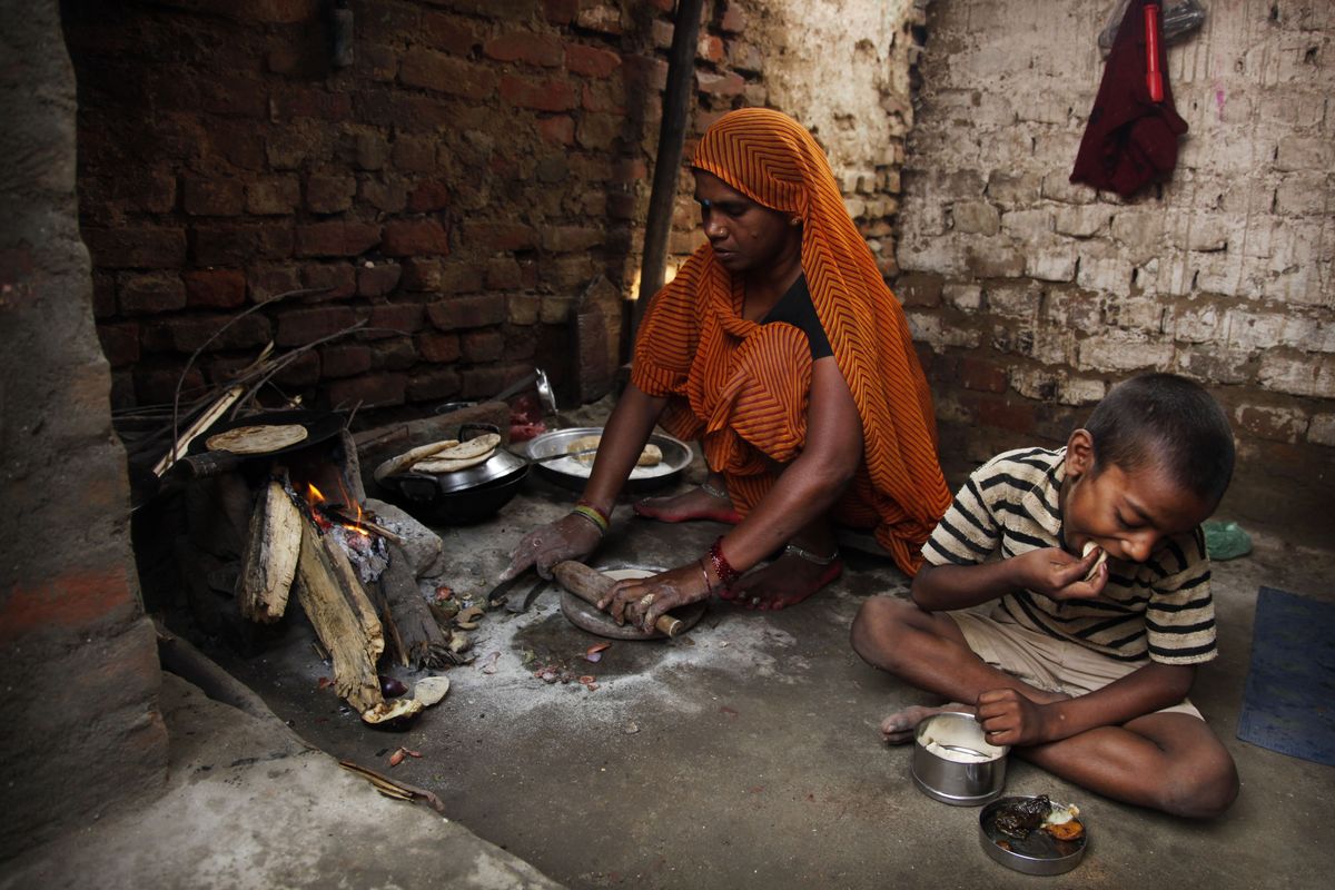 A woman prepares chapati, a traditional bread made with wheat flour, by the fireside as her son eats a meal at their home in Allahabad, India. Agronomists say rising temperatures from global warming are reducing India’s wheat crop.  (Associated Press)