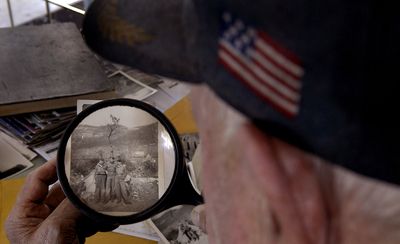 Dane Broadfoot, of Post Falls, uses a magnifying glass to identify himself as the man in the center of this picture taken during World War II in Cassino, Italy.  (Kathy Plonka / The Spokesman-Review)