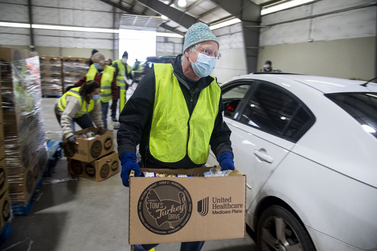 Volunteer John Whalen carries a box of Thanksgiving food to a car in line inside an agricultural building at the Spokane County Fair and Expo Center, Tuesday, Nov. 24, 2020.   (Jesse Tinsley/The Spokesman-Review)