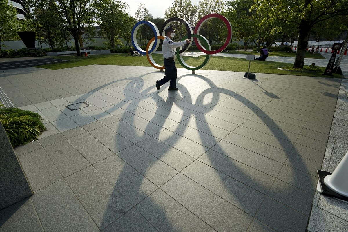 FILE - In this May 9, 2021, file photo, a security guard wearing a protective mask to help curb the spread of the coronavirus walks in front of the Olympic Rings, in Tokyo. Japan, seriously behind in coronavirus vaccination efforts, is scrambling to boost daily shots as the start of the Olympics in July closes in.  (Eugene Hoshiko)