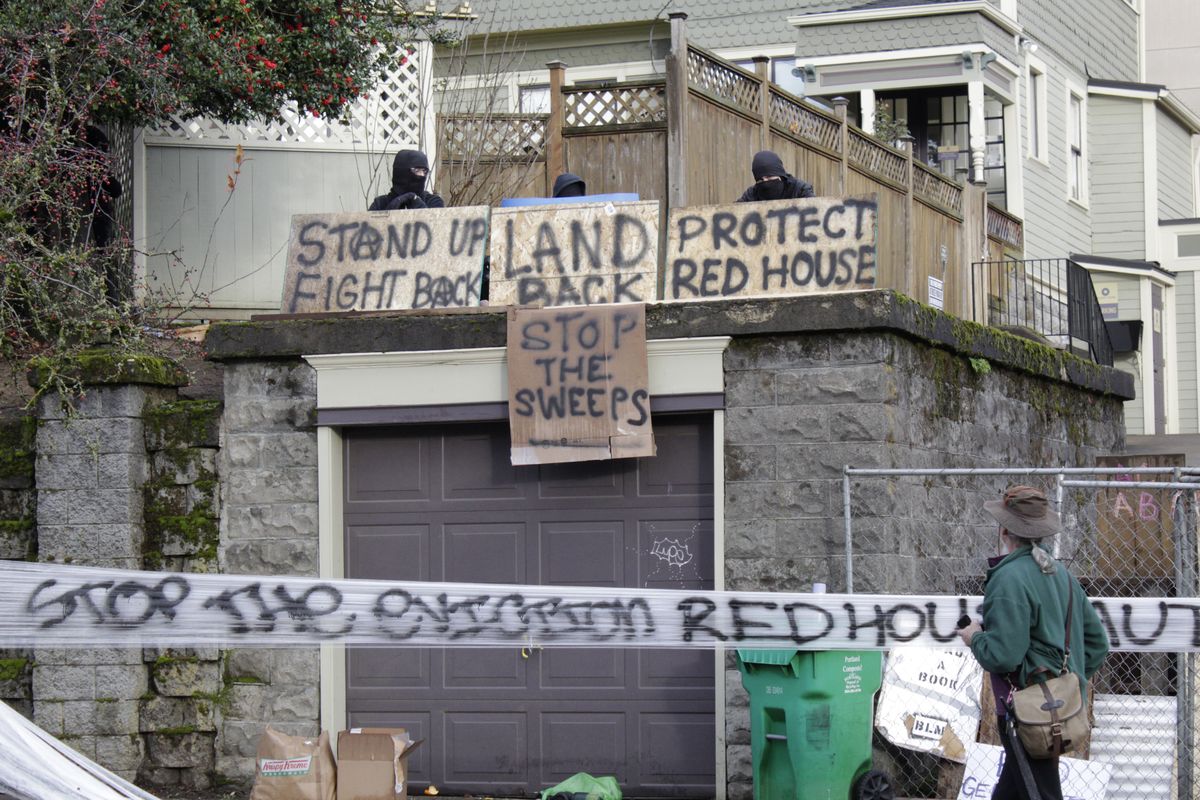 FILE - Masked protesters by an occupied home speak with a neighborhood resident opposed to their encampment and demonstration in Portland, Ore., on Dec. 9, 2020. Growing discontent over homelessness, crime and protests in Portland is driving interest in a pair of congressional primaries in the state.  (Gillian Flaccus)