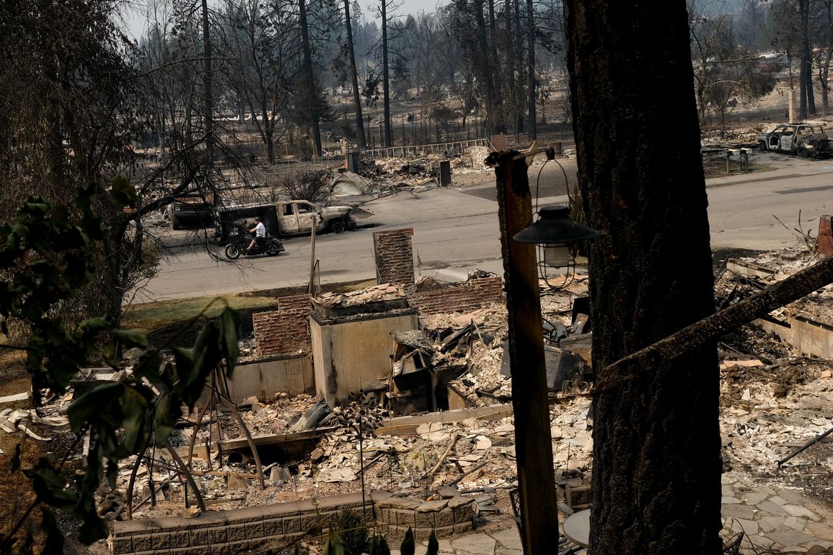 A man rides a motorcycle along West Rifle Club Road while looking at the damage from the Old Trails fire on Monday in Spokane. (Tyler Tjomsland/The Spokesman-Review)