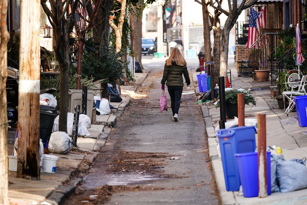 A woman walks past trash that is sitting out for collection in Philadelphia, Thursday, Jan. 13, 2022. The omicron variant is sickening so many sanitation workers around the U.S. that waste collection in Philadelphia and other cities has been delayed or suspended.  (Matt Rourke)