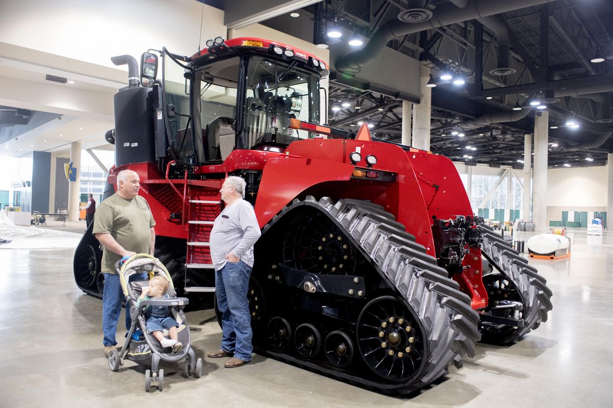 Brad Shrum, left, with his grandson Wyat Shrum, age 19 months, chats with Bob Kerns beside a large Case tractor during the setup of the annual Ag Trade Show at the Spokane Convention Center. (Jesse Tinsley / The Spokesman-Review)