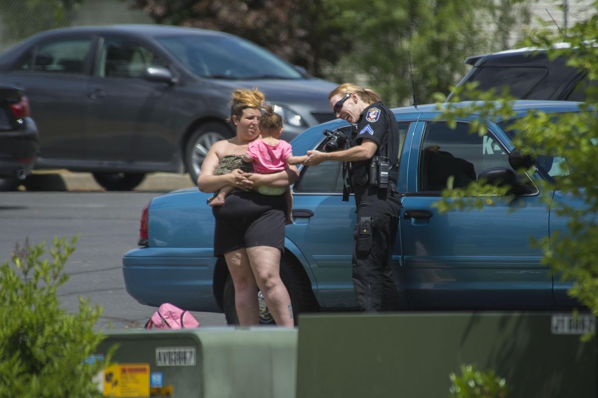 A Spokane police officer checks on a child that was involved with a hostage standoff Wednesday near the corner of Morton Court and West View Court. (Dan Pelle / The Spokesman-Review)