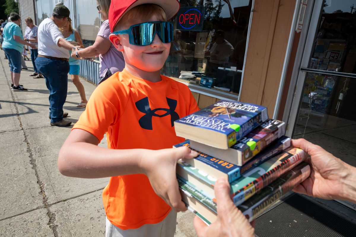 In a human chain, Barrett Ponzoha, 7, helps pass the books from the Rosalia Library's temporary location in the community center up the street to the new building in downtown Rosalia, Tuesday, August 6, 2024. Last year, the Rosalia Library’s basement flooded forcing it to relocate and operate temporarily in the Rosalia Community Center. Back in May 2024, Pat Voge, owner of Pat’s Books, generously donated her building to the Town of Rosalia with the plan of having the Rosalia Library move in to the building.  (COLIN MULVANY/THE SPOKESMAN-REVIEW)