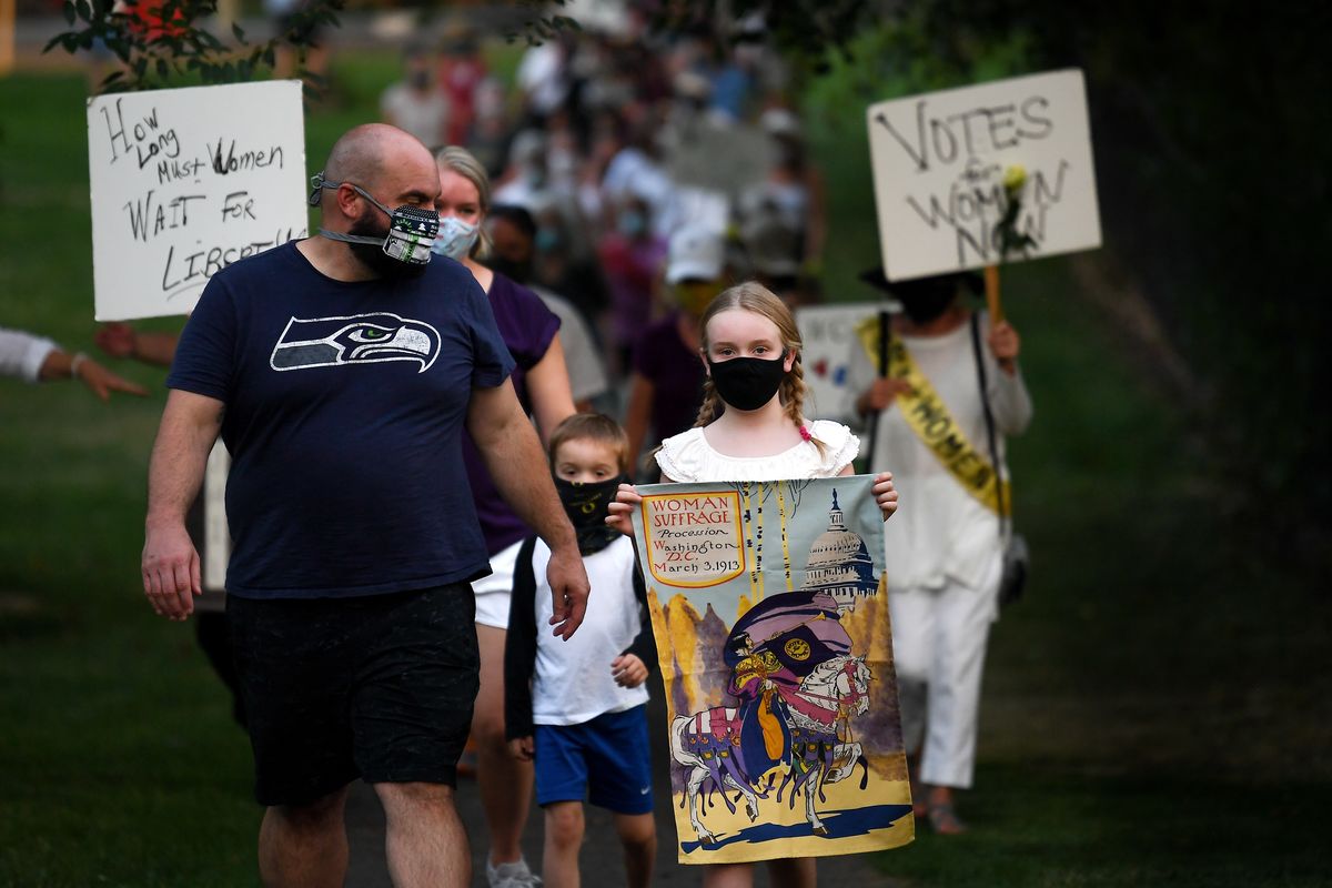 Olivia Vehrs, 9, center, marches in front of a crowd next to her mother Hannah Vehrs, second left, and her soon-to-be-stepfather, Jeff Harris, left, during a Silent Suffrage March on Tuesday at Polly Judd Park. (Tyler Tjomsland/THE SPOKESMAN-REVIEW)